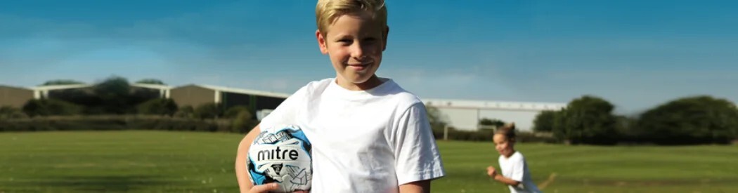 child holding football on football pitch
