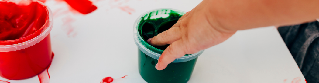 child tipping their hand into a pot of green paint