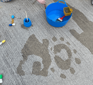 child practising water writing outdoors with pouring utensils