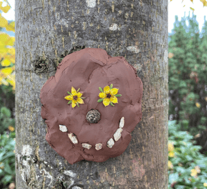 child placing natural materials into clay face sculpture outside