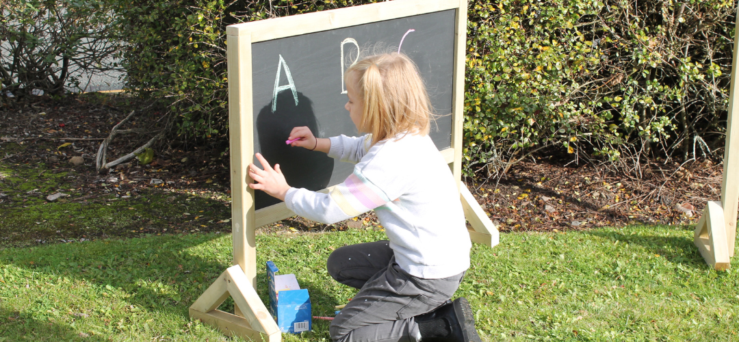 child forming letters using chalk sticks on chalkboard