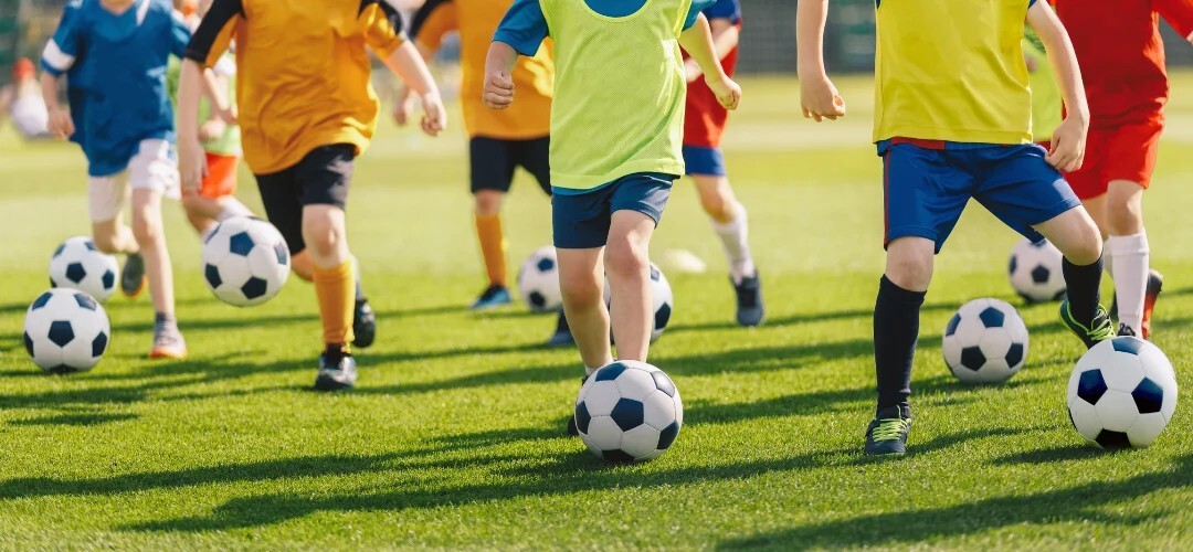 children dribbling football on astroturf