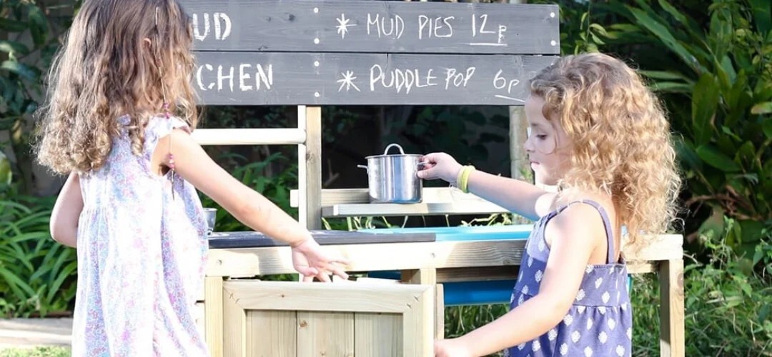 two children playing with mud kitchen equipment