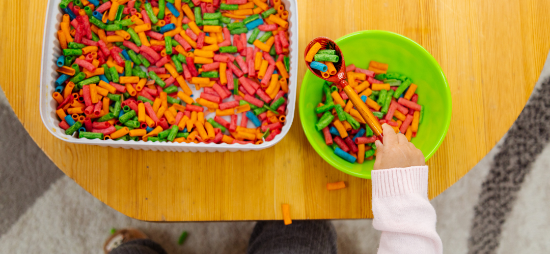 baby playing with coloured pasta shapes