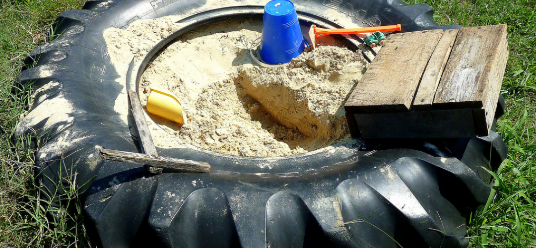 Large tractor tyre filled in the centre with sand and various sand play accessories