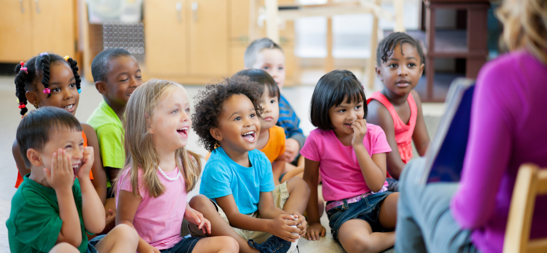 group of children sat on the floor smiling at a teacher