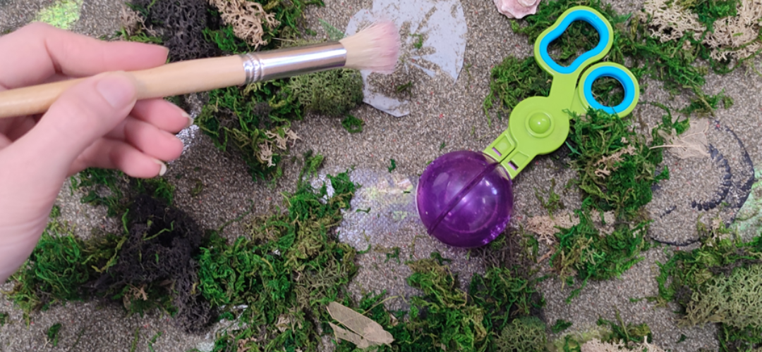 Image shows a hand brushing sand off toy fossils