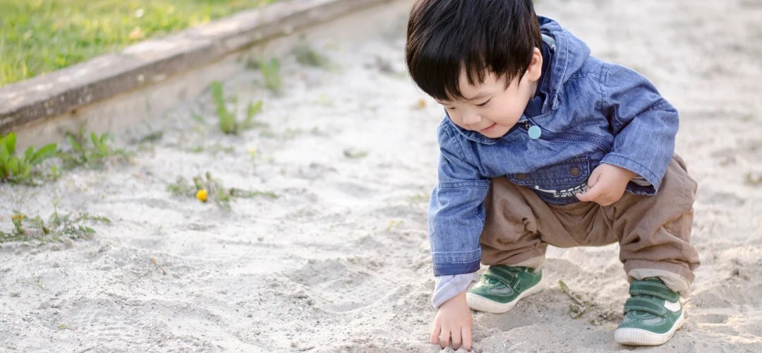 child investigating sand in sand pit