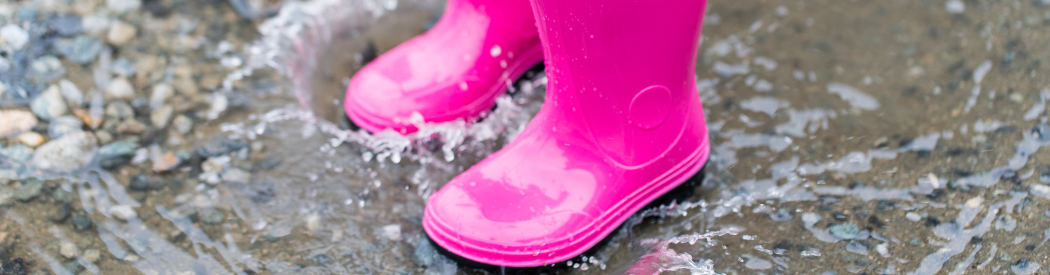 children splashing in puddle with pink boots outdoors