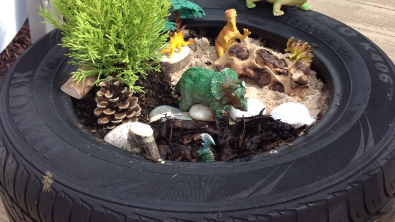 large tyre filled with wood chips and sand and featuring small world dinosaur toys