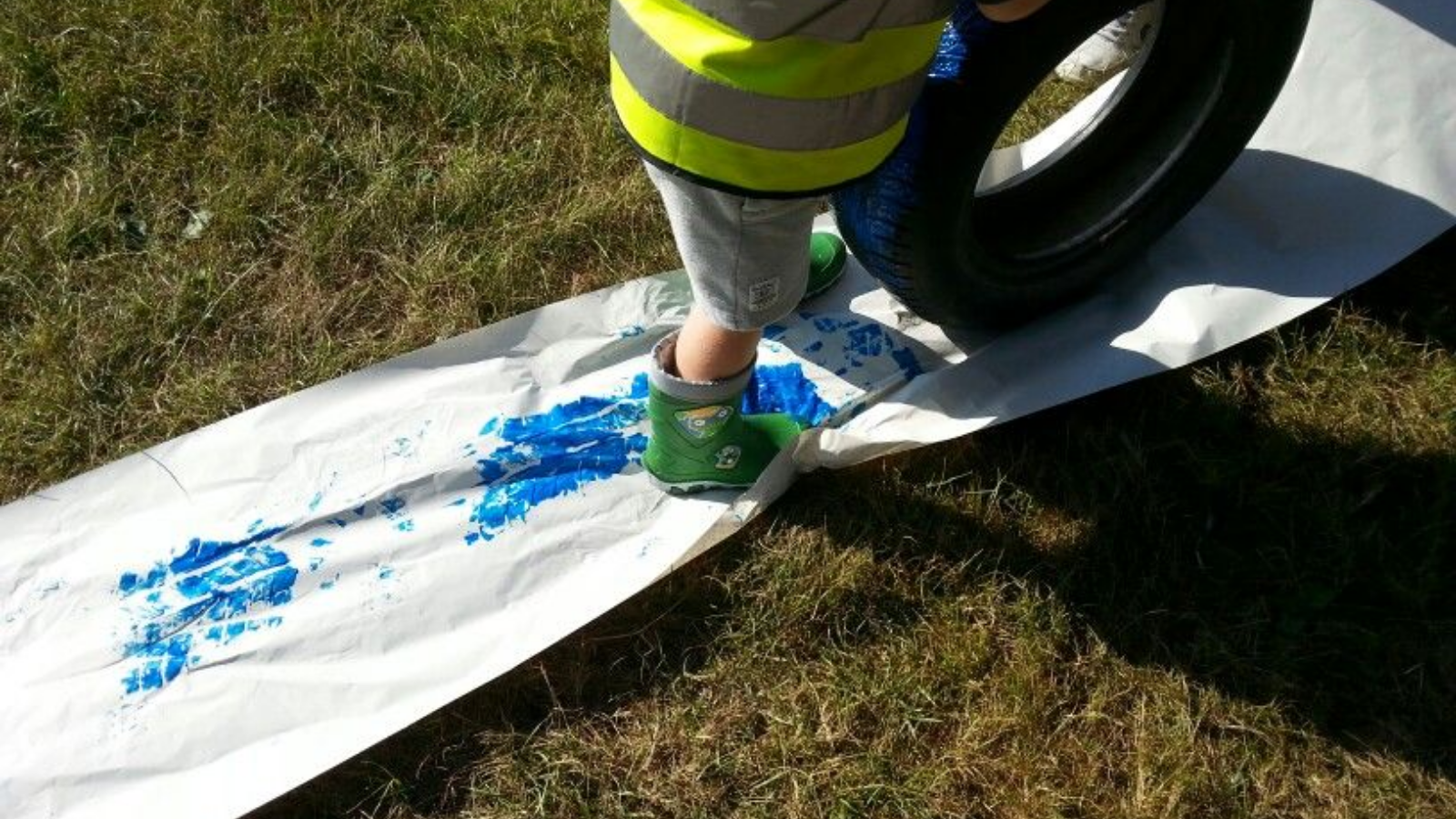 a child rolling a tyre covered in paint along a strip of white material